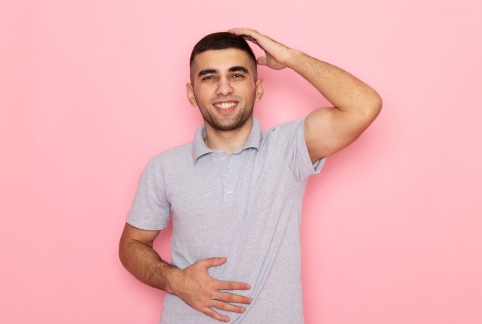 Un jeune homme sourit sereinement, une main posée sur son ventre et l'autre sur sa tête