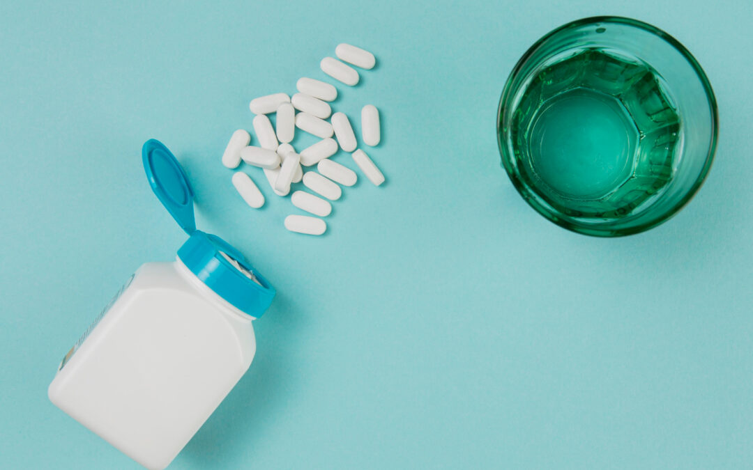 Une boîte de compléments alimentaires posée sur une table à côté de gélules et d’un verre d’eau